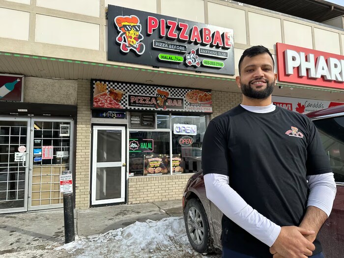 Un homme souriant se tient devant une pizzéria, à Calgary, 2026.
