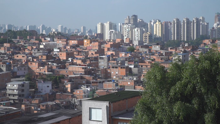 Vue sur plusieurs petites maisons au pied de gratte-ciels plus imposants à Sao Paulo.