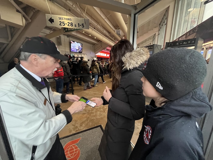 À l'intérieur de l'aréna, un employé scanne le téléphone d'une femme qui montre son billet.