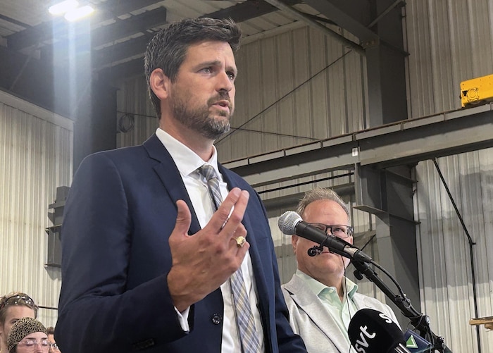 Sean Fraser est debout dans ce qui semble être un hangar et il lève la main gauche.