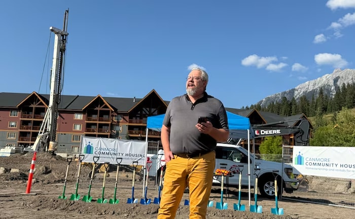 Un homme, téléphone à la main, se tient sur un chantier de construction, avec des pelles derrière lui, à Canmore, en Alberta, en septembre 2025.