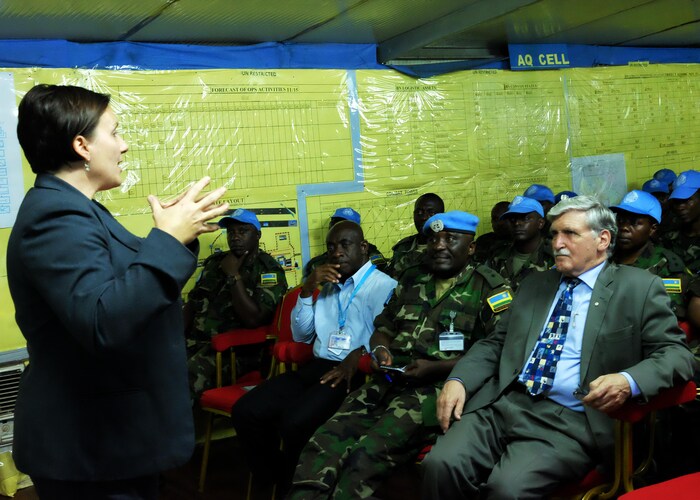 Shelly Whitman debout devant Roméo Dallaire, assis au centre de militaires rwandais en uniforme.