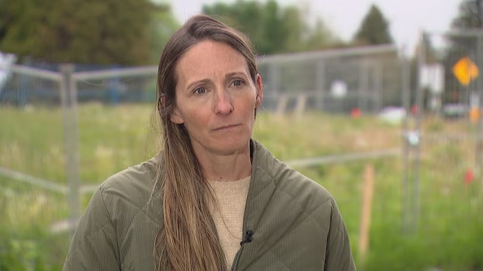 Une femme fixe du regard l'objectif d'une caméra alors qu'elle se tient devant une clôture de barbelés, à Edmonton, en Alberta.