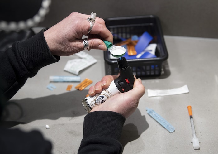Une femme assise dans un cubicule chauffe de la drogue à l'aide d'un briquet et d'une cuillère.