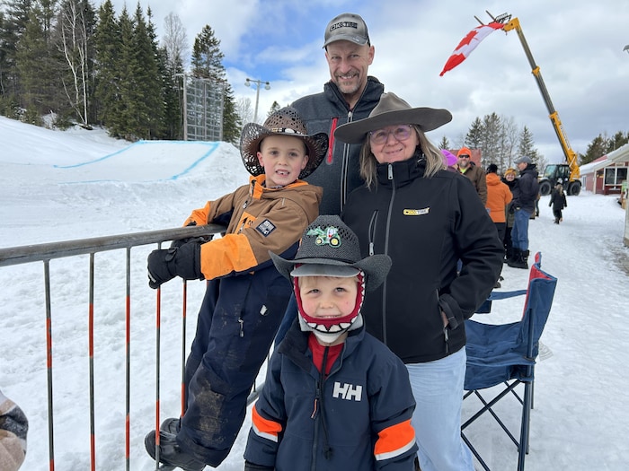 Un homme, une femme et deux garçons de moins de 10 ans posent pour une photo de famille au centre de ski, devant une barrière en métal.