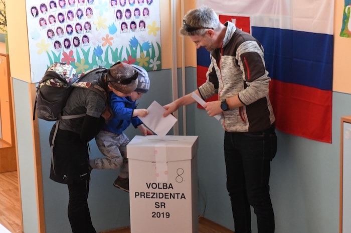 Un homme et une femme, accompagnés de leur enfant, déposent un bulletin de vote dans une boîte électorale.
