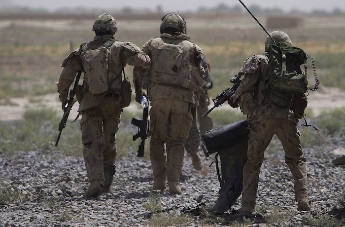 Trois militaires, vus de dos, marchent l'arme à la main.