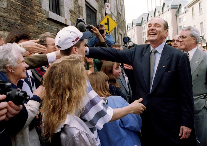 La bouche ouverte, Jacques Chirac est debout devant des dizaines de badauds dans la rue et serre des mains.