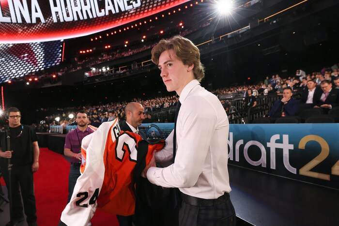 Spencer Gill, debout dans un amphithéâtre pour le repêchage, s'apprête à enfiler un chandail de hockey orange.