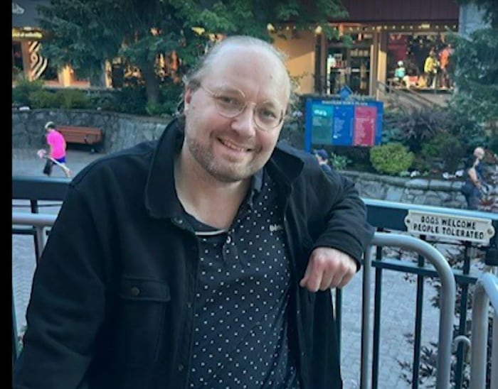 Un homme darborant un sourire fixe l'objectif d'une caméra.
