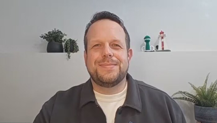 Un homme esquisse un sourire devant l'objectif d'une caméra.