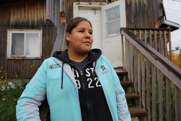 Une jeune autochtone prend la pose devant sa maison qui a besoin de rénovation.