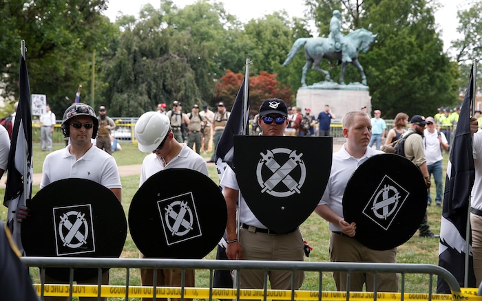 Quatre hommes habillés en blanc tiennent des boucliers noirs à l'insigne de Vanguard America.