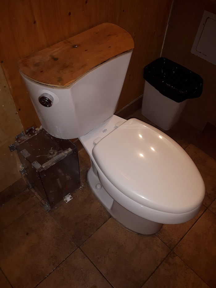 Le réservoir de la toilette est recouvert de contreplaqué, ainsi que le mur derrière.