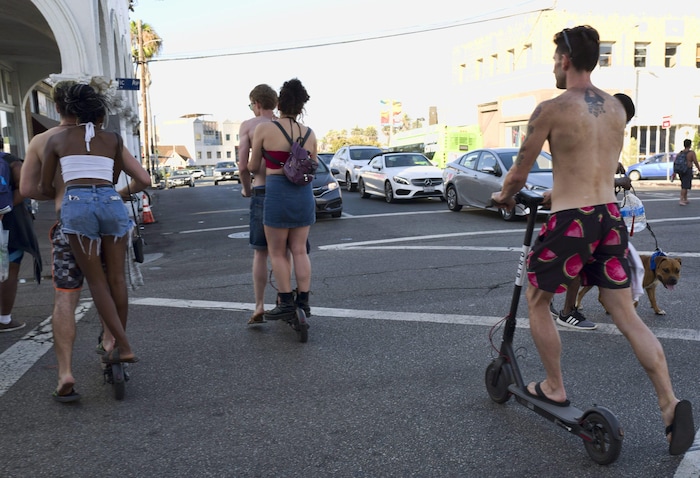 Deux couples partagent une trottinette électrique et un autre homme torse nu et portant un short décoré de dessins de tranches de melon d'eau circule seul sur une autre.