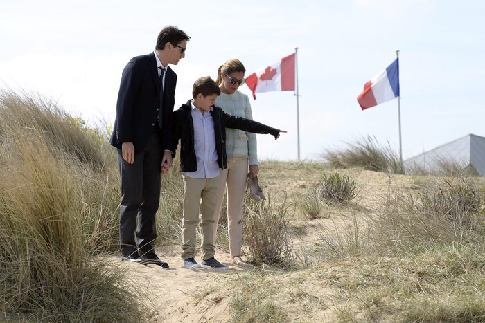 Justin, Xavier et Sophie Trudeau sur la plage Juno avec en arrière plan les drapeaux canadien et français.