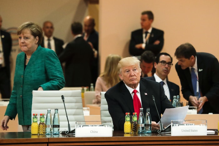 Donald Trump est assis seul alors que la chancelière allemande, Angela Merkel, marche derrière lui. 
