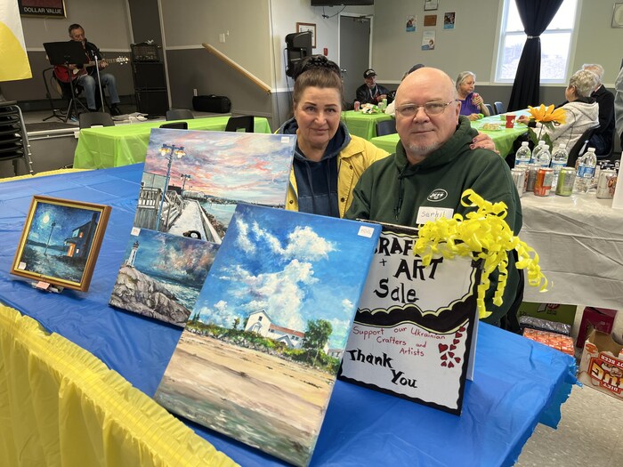 Un couple assis à une table sur laquelle sont disposées plusieurs peintures de différentes grandeurs.