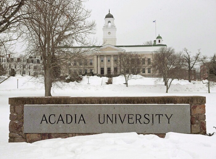 Bâtiment et enseigne de l'Université Acadia entourés de neige en hiver.