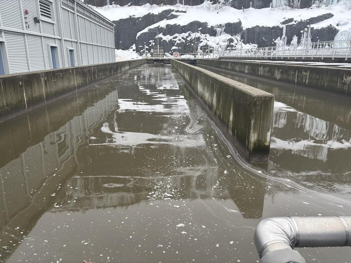Un grand réservoir d'eau d'une usine de filtration, à l'extérieur, avec une colline enneigée derrière.