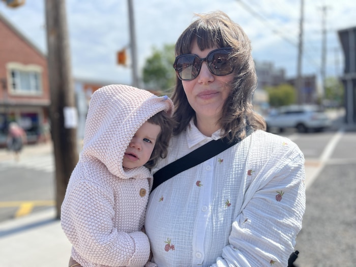 Une femme avec des lunettes fumées tient sa petite fille dans ses bras.