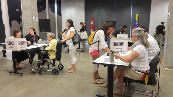 Plusieurs personnes remplissent leur bulletin de vote, qu'ils déposent ensuite dans une boîte où on peut lire « Le peuple décide! »