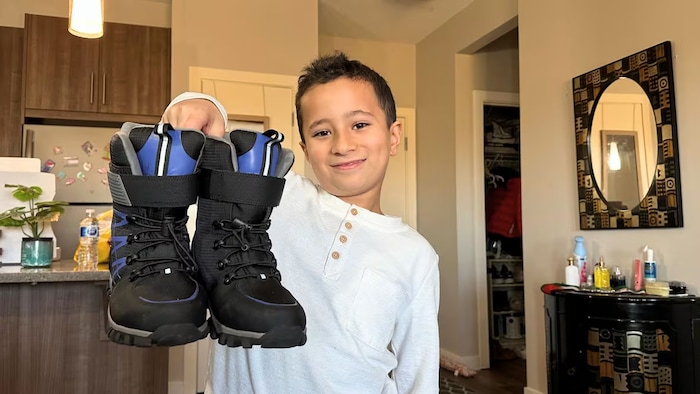Un jeune garçon montre fièrement ses nouvelles bottes de neige.