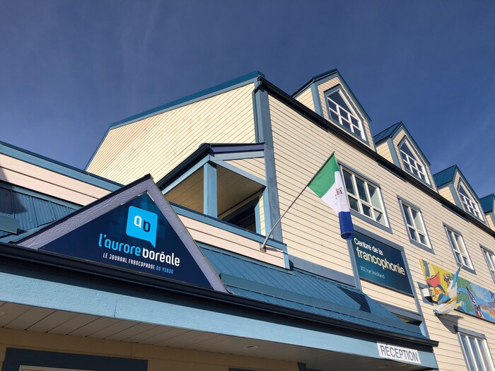 Façade d'un édifice avec la bannière du journal et un drapeau du Yukon.