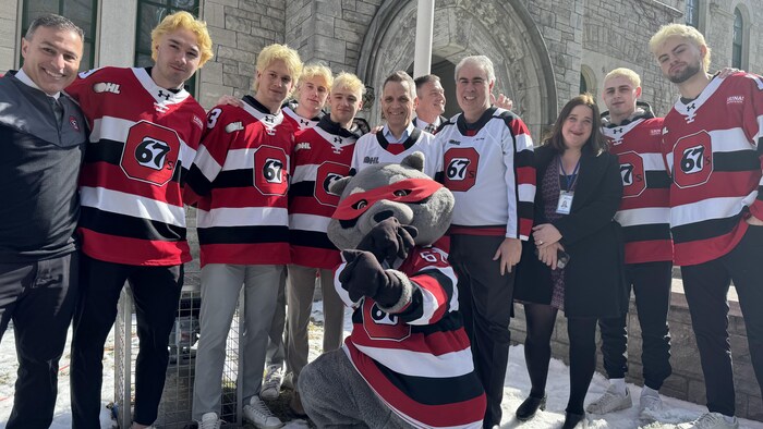 Des joueurs de hockey prennent la pose avec un politicien après avoir vu leur drapeau être hissé devant l'hôtel de ville.