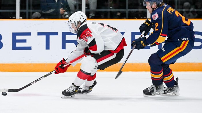 Un joueur de hockey protège la rondelle pendant un match alors que son adversaire tente de le ralentir.