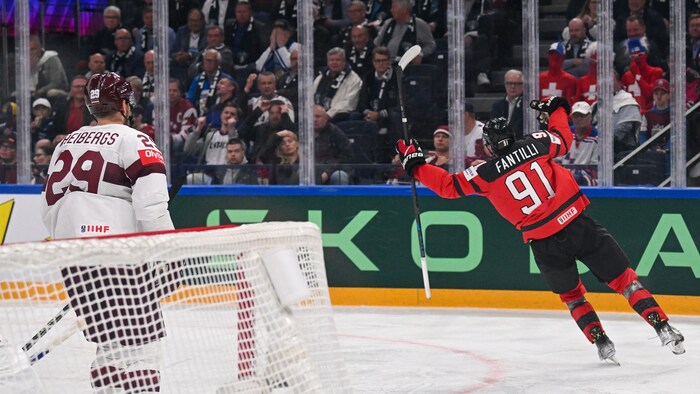Un hockeyeur canadien lève les bras pour célébrer un but devant un adversaire letton.