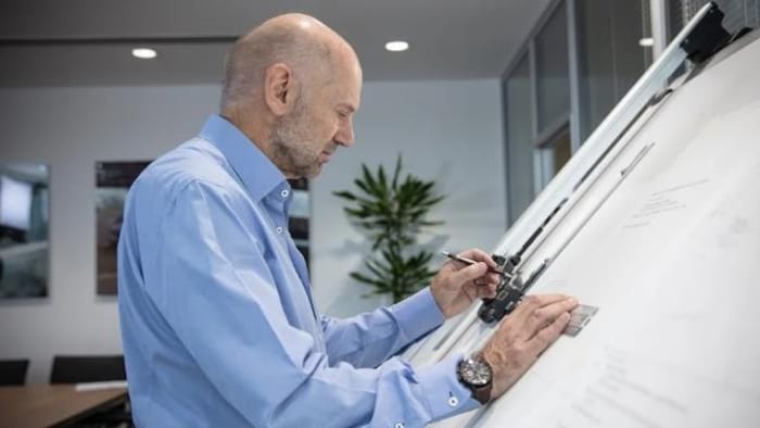 Un homme gaucher, en chemise, de profil, dessine avec un crayon.