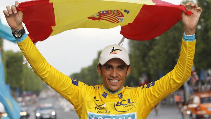 Alberto Contador porte le maillot jaune et célèbre sa victoire du Tour de France 2010 en soulevant un drapeau de l'Espagne au-dessus de sa tête, sur les Champs-Élysées, à Paris.
