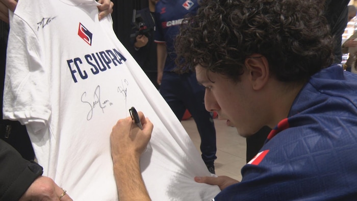 Un jeune homme signe un chandail avec un logo d'une équipe de soccer.