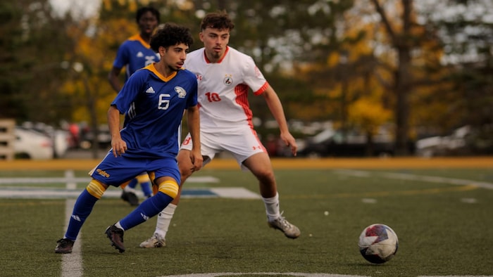 Un joueur se dirige vers le ballon et un adversaire, derrière lui, le regarde faire.