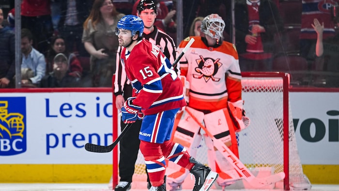 Un joueur de hockey patine devant un arbitre et un gardien de but.