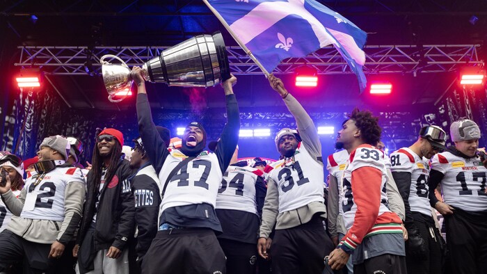 Un joueur brandit un drapeau du Québec, tandis qu'un autre soulève la coupe Grey.