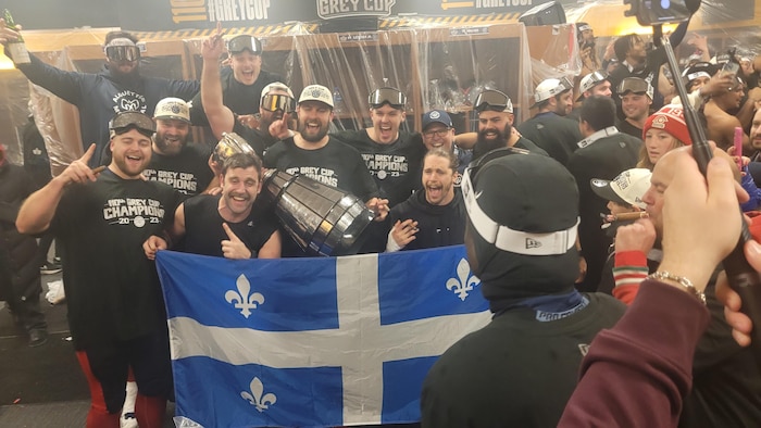 Des joueurs des Alouettes posent avec la coupe Grey derrière un drapeau du Québec.