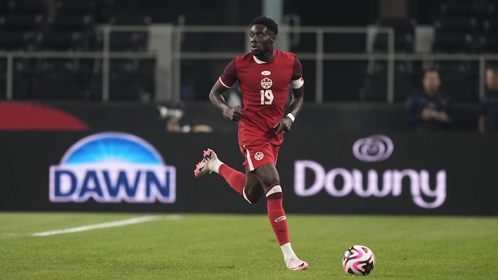 Un joueur de soccer en rouge court avec le ballon à ses pieds.