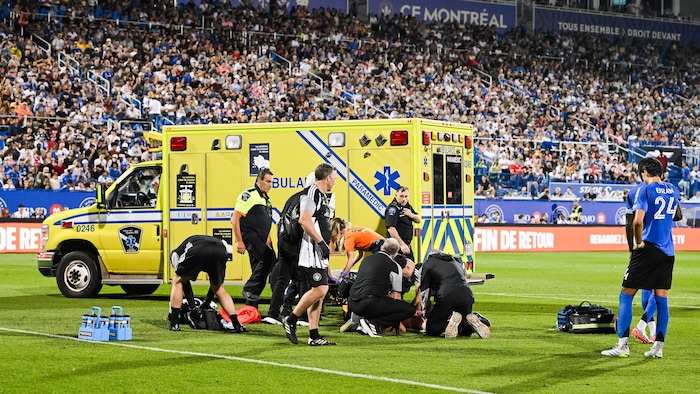 Des ambulanciers et du personnel médical entourent un joueur de soccer au sol.