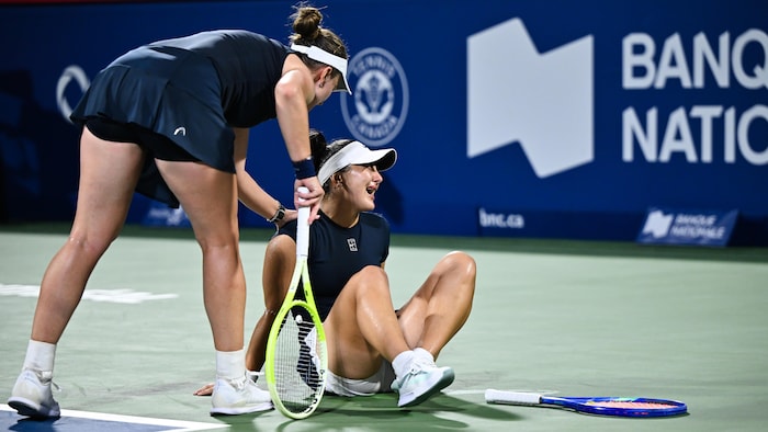 Une joueuse de tennis en console une autre assise sur le terrain et visiblement en douleur. 