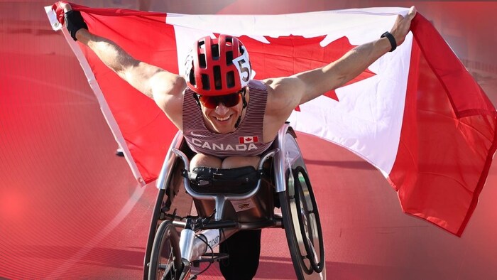 L'homme en fauteuil roulant tient le drapeau canadien derrière lui.