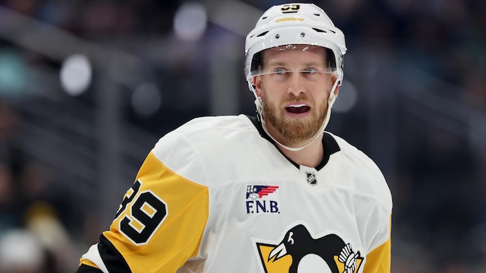 Vêtu de l'uniforme des Penguins de Pittsburgh, il regarde au loin.