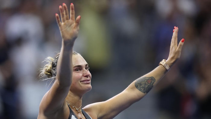 Une joueuse de tennis salue la foule avec les deux bras dans les airs. 
