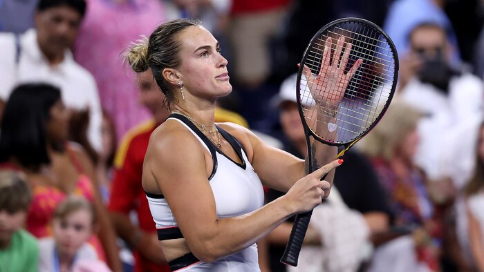 Une joueuse de tennis applaudit la foule avec sa raquette.