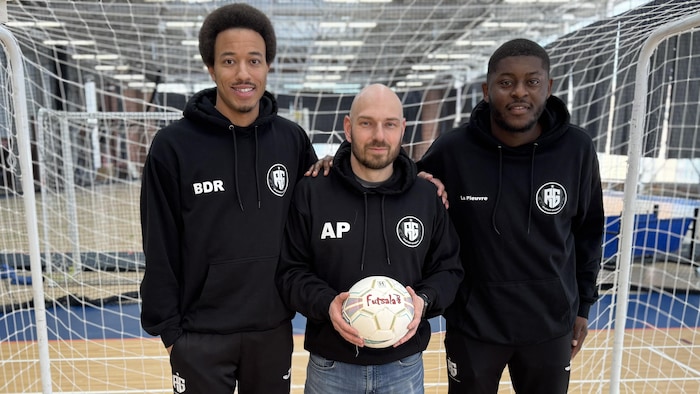 Trois hommes prennent la pose avec un ballon de futsal devant un filet.