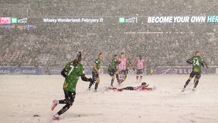 Un joueur de soccer est au sol dans la neige après avoir été bousculé sur le terrain.