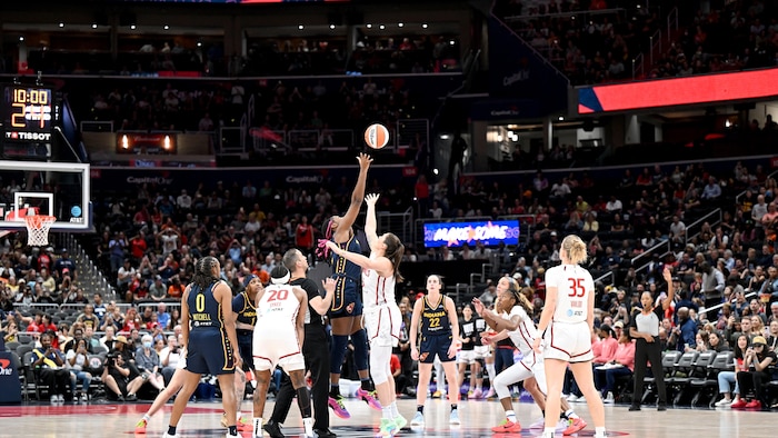 Professional basketball players jump for the ball during a game's faceoff in front of a record crowd.