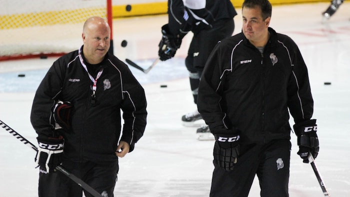 Deux entraîneurs de hockey patinent sur une glace pendant un entraînement.