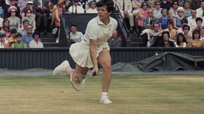Billie Jean King frappe un coup pendant un match, devant des gradins remplis de spectateurs.